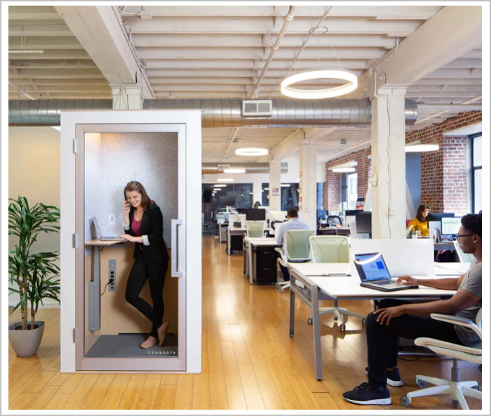 Innovative office furniture example - A person on a call inside a small phone booth in an office with people sitting at desks