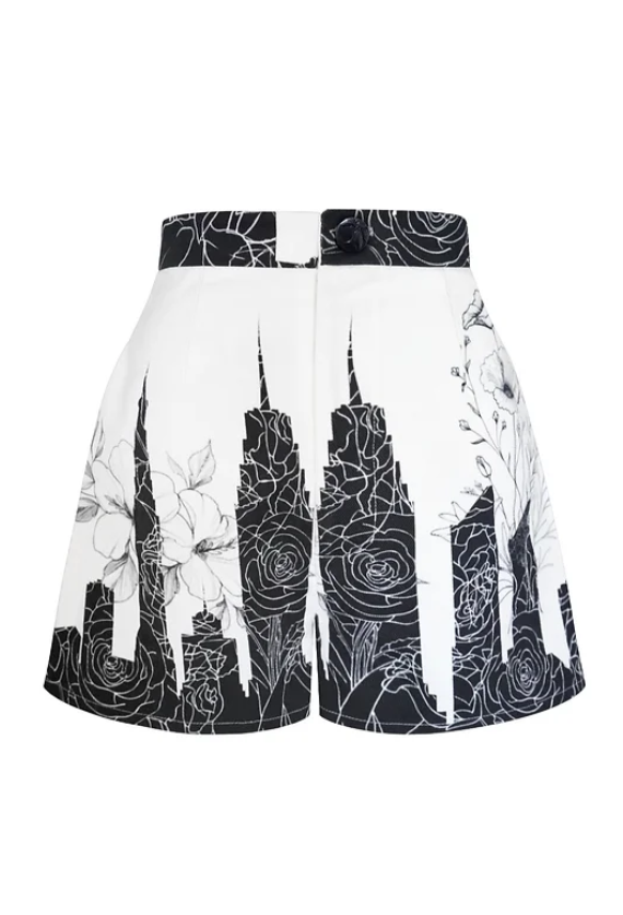 A pair of white shorts with black and white floral and cityscape print against a white background.