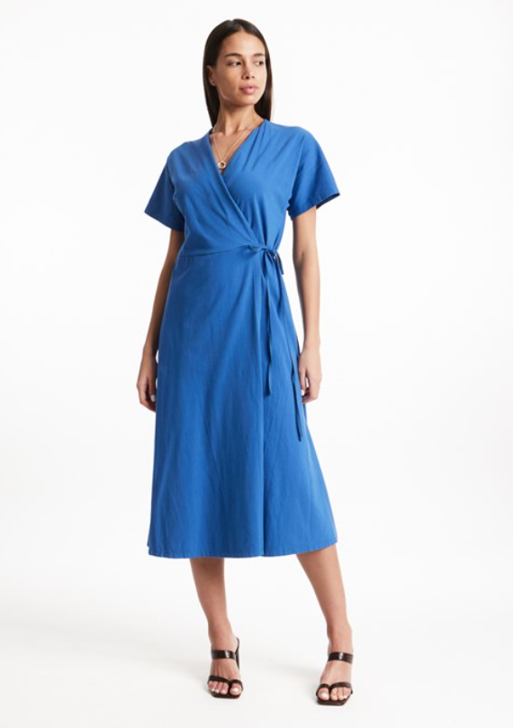 Woman wearing a blue below-the-knee length short-sleeved wrap dress and black strappy high-heeled sandals.