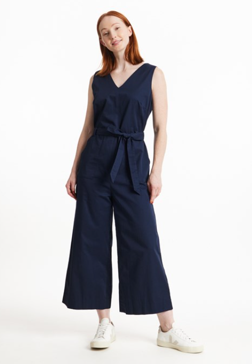 : Sustainable apparel companies example - Woman wearing a sleeveless navy jumpsuit and a pair of white sneakers.