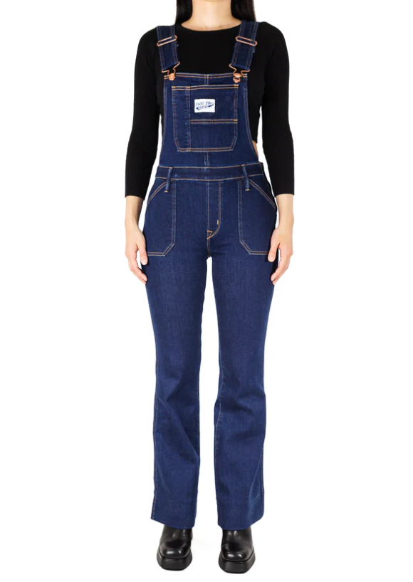 Person wearing a blue form-fitting denim overalls. They’re wearing a black long-sleeved crop top shirt under.