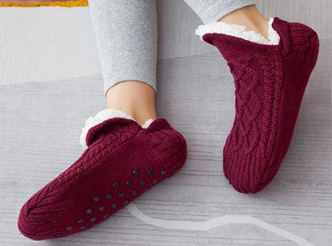A pair of cozy red unisex slippers with fuzzy lining, perfect for keeping your feet warm and comfortable.