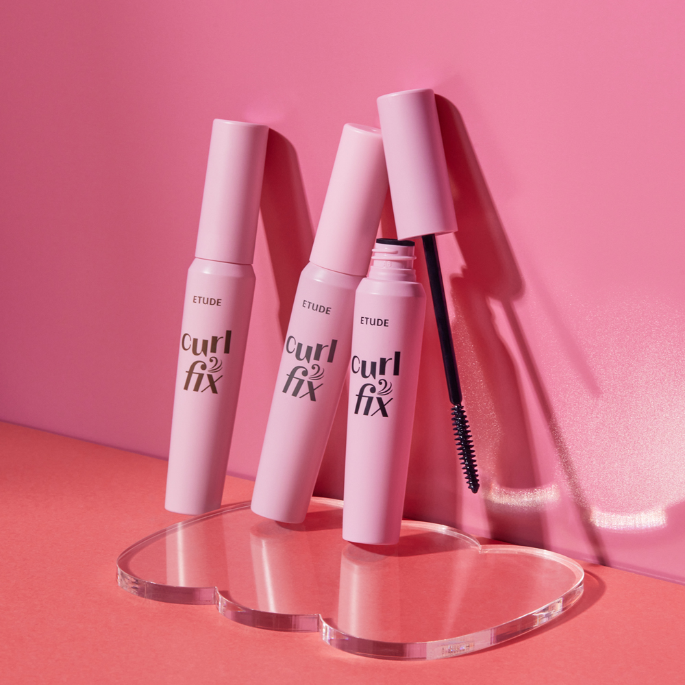 The ETUDE Curl Fix mascara is placed on a surface that is pink in color.