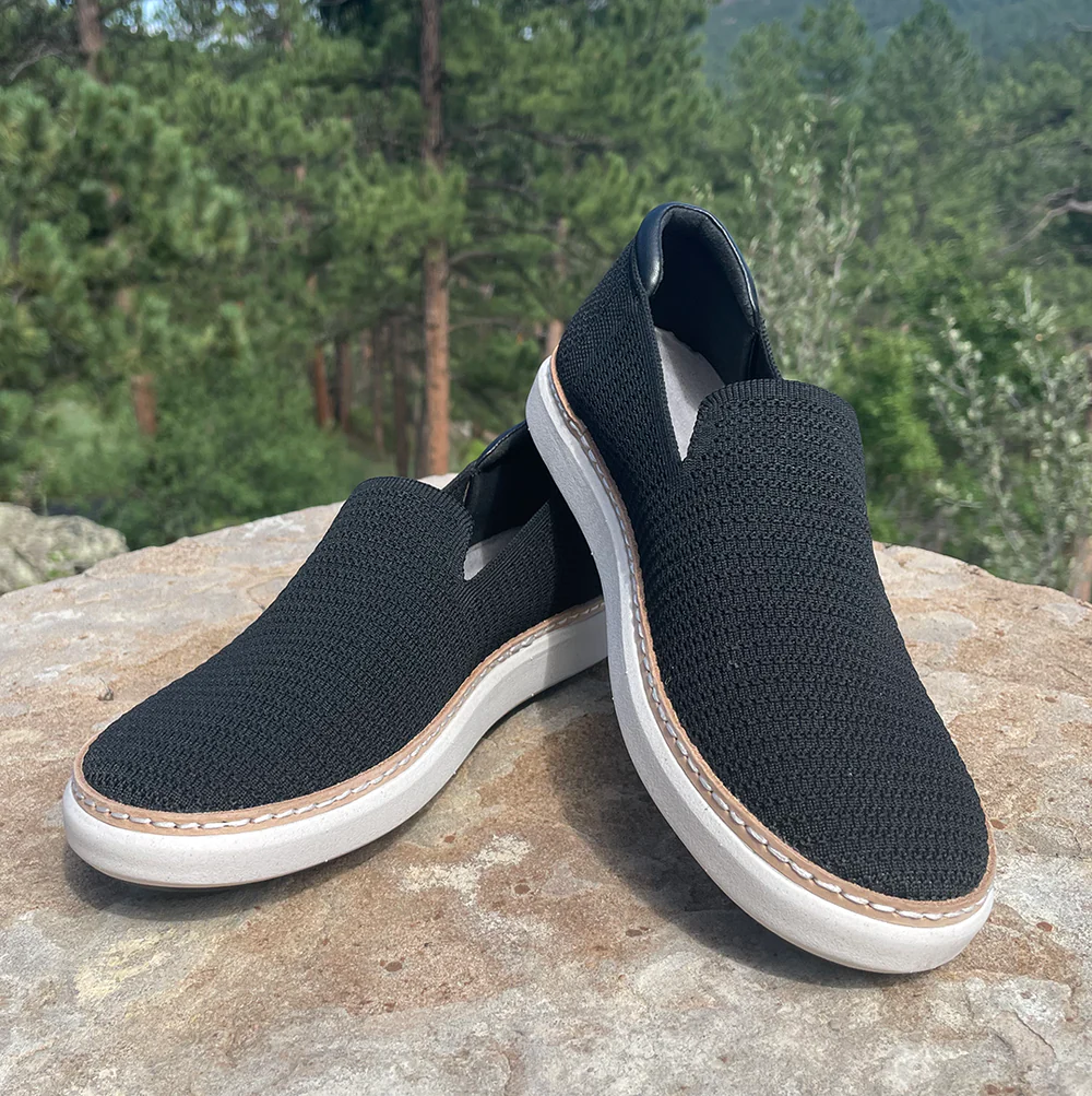 A pair of black slip-on sneakers resting on a rocky surface.