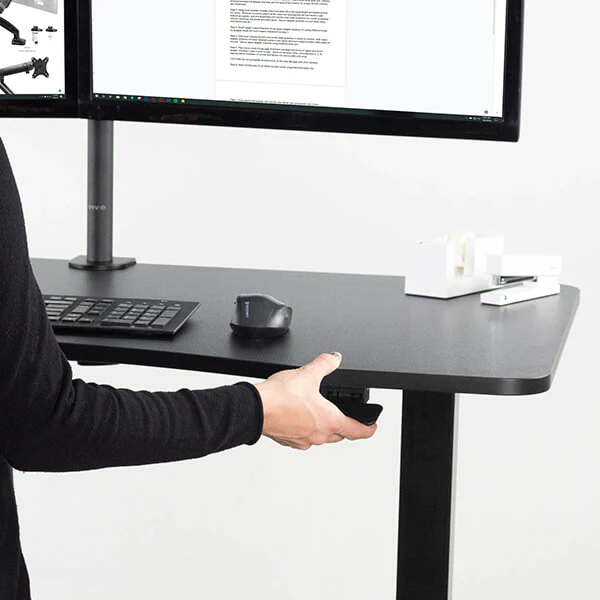 A man in black sleeves adjusts his black standing desk.