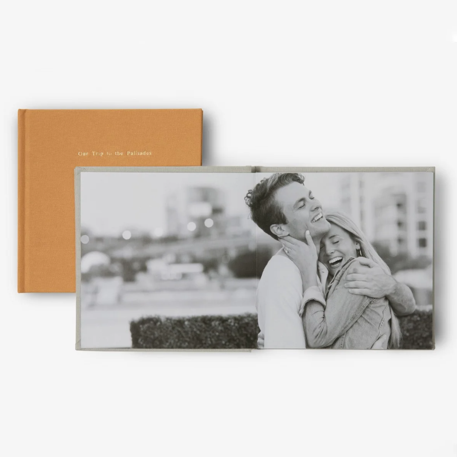 Small square photo book with a linen cover and foil-stamped title, opened to thick pages displaying personal photographs as meaningful personalized gifts.