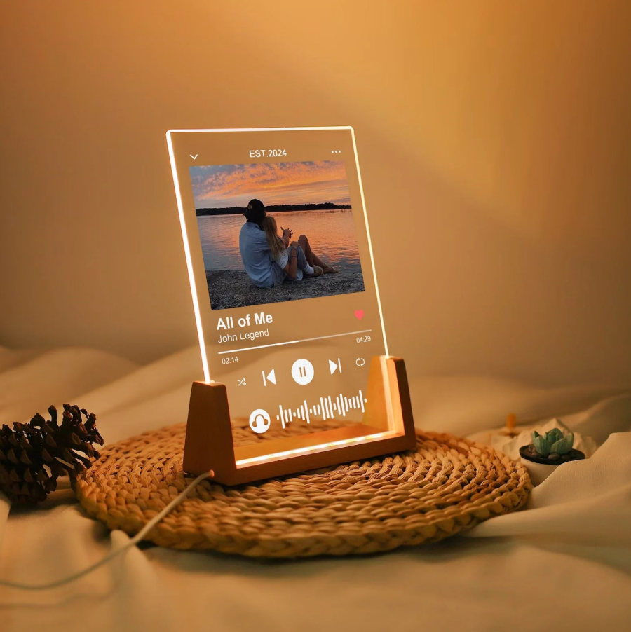 Personalized acrylic night light with a photo and song information illuminated on a wooden base, offered through custom gift services.